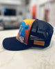 Blue trucker hat featuring bear with foe leather patch 'Alaska' patch on a blurred background