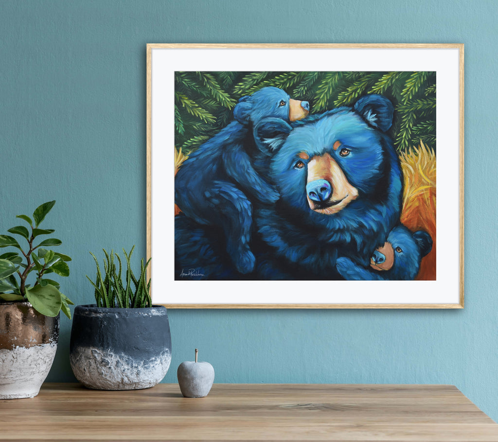Framed artwork of three bears on a wall with decorative plants and a wooden table.