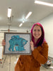Amanda Rose Warren holding a framed artwork of a blue momma bear and babies in an indoor setting