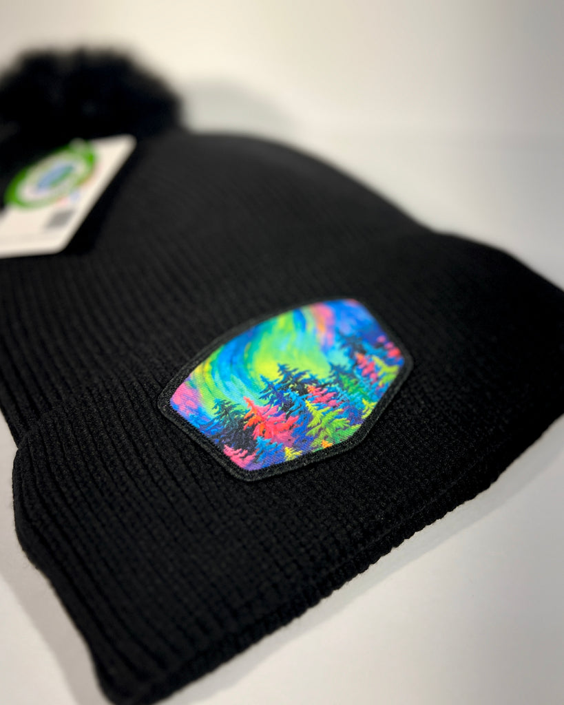 Alaska Mystic Tree pom beanie with fleece lining, showcasing vibrant rainbow forest artwork and warm cozy winter style