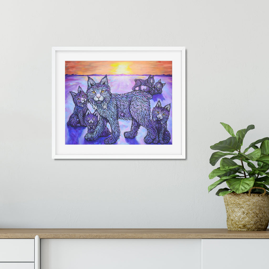 Framed artwork of a lynx and kittens against a purple sky with a plant on a shelf below.