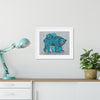 Framed artwork of blue bears on a white wall above a wooden shelf with a lamp and plant.