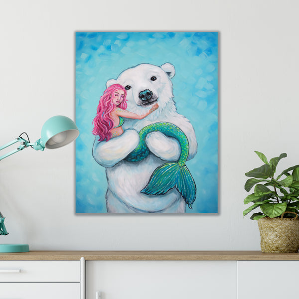 Art print of a polar bear and mermaid on a wall above a desk with a lamp and plant.