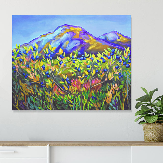 Colorful abstract painting of a mountain landscape on a white wall with a plant below.