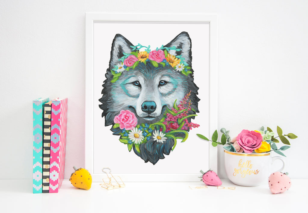 Framed artwork of a wolf with floral crown on a white surface with decorative items.