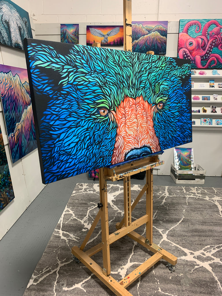 Alaskan bear with fun and vibrant blue and green fur sitting on an easel with other beautiful works of art in the background 